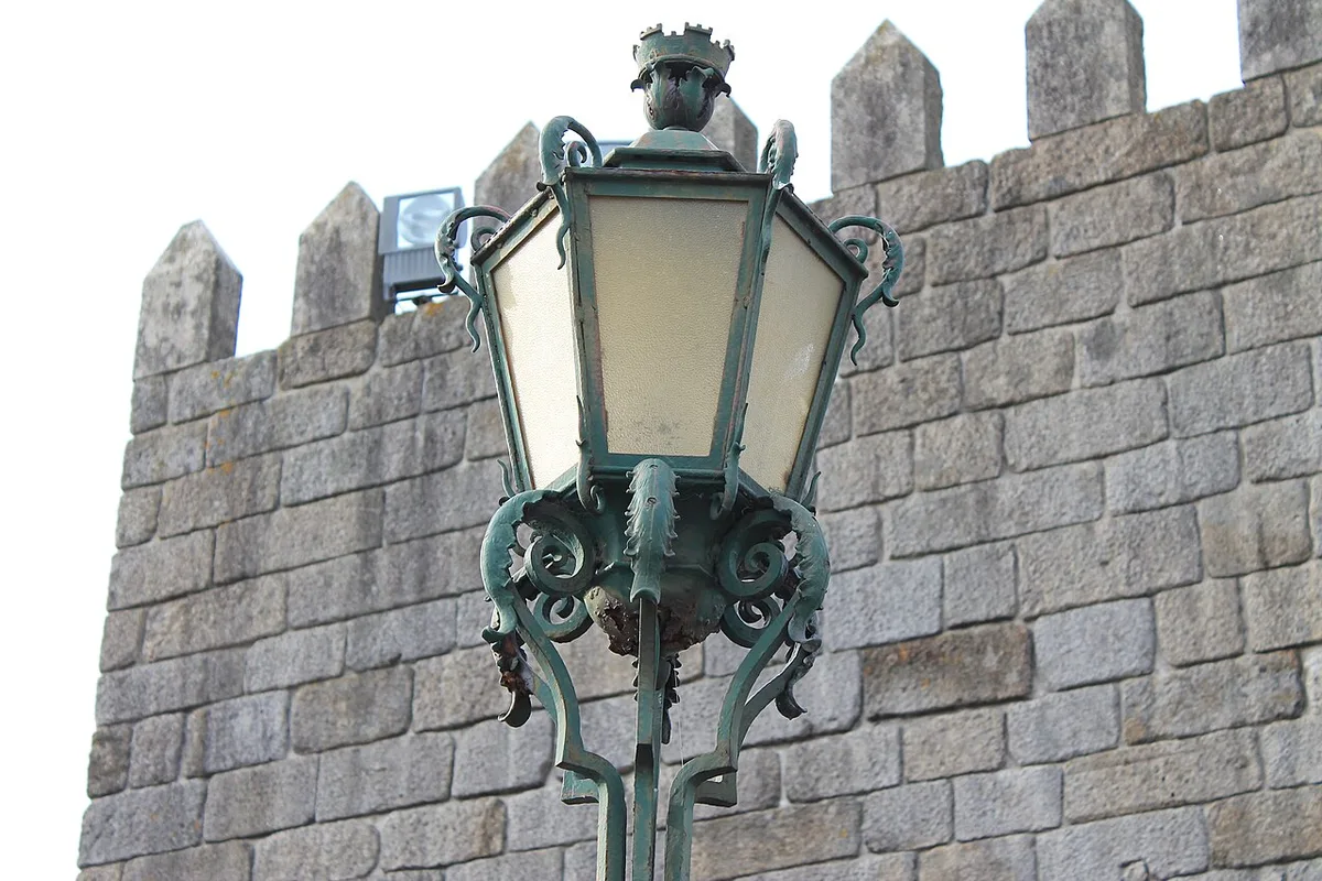 Ornate street lamp in front of a crenellated stone wall in Porto