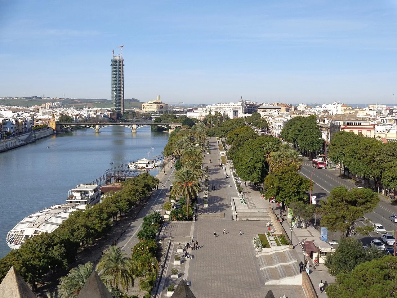 Historical view along Seville's riverside promenade toward Triana Bridge
